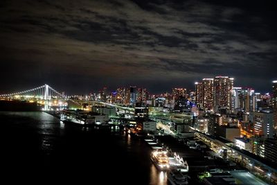 Illuminated city by sea against sky at night