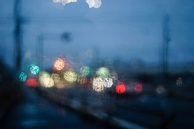 Defocused image of illuminated street seen from wet glass window at night