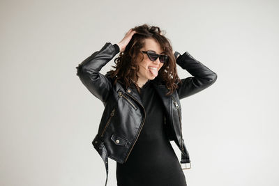 Brunette with curly hair, glasses and leather jacket shows her tongue isolated