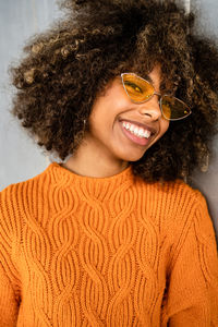 Beautiful cheerful ethnic woman with curly afro hair wearing vivid orange sweater looking at camera against gray wall