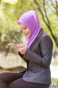 Young woman wearing hijab using mobile phone while sitting in park