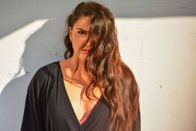 Portrait of beautiful young woman standing against wall