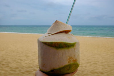 Close-up of hand holding drink at beach against sky