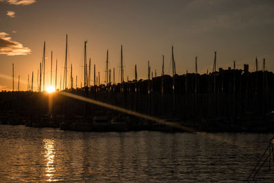 Silhouette sailboats by river against sky during sunset