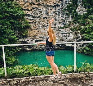 Young woman standing by pond against rock formation