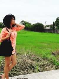 Young woman standing on field against sky