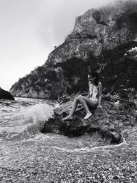 Portrait of woman sitting on cliff against mountains