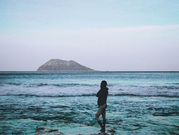 Rear view of woman standing at beach against sky