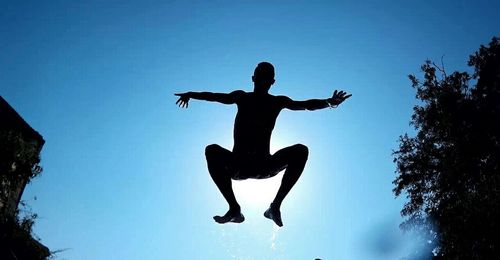 Low angle view of woman jumping against blue sky