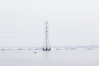 Electricity pylons on snow covered landscape against clear sky