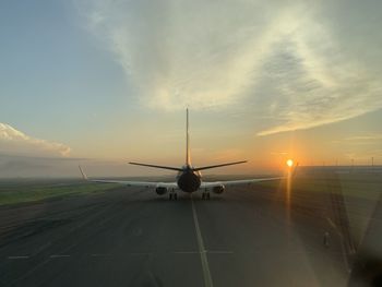 Airplane on runway against sky during sunrise