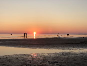 Silhouette people on beach against sky during sunset