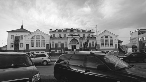 Cars on road by buildings in city against sky