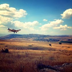 Airplane flying over landscape against sky