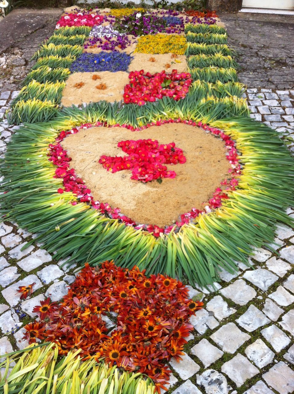 HIGH ANGLE VIEW OF MULTI COLORED FLOWER ON COBBLESTONE