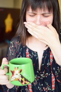 Young woman making face while holding cup