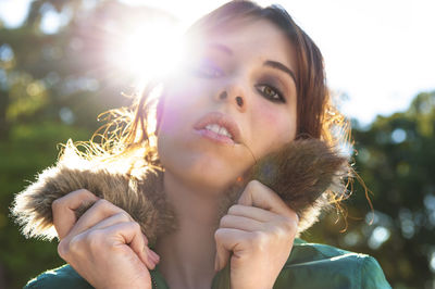 Close-up portrait of young woman in warm clothing against sky at park during sunny day