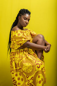 Portrait of young, beautiful woman sitting on a wooden stool. against yellow background.