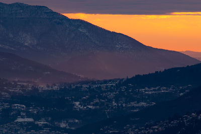 Aerial view of townscape and mountains against sky at sunset