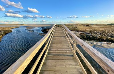 Surface level of boardwalk leading towards sea against sky