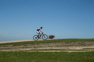 Man riding bicycle on field against clear sky