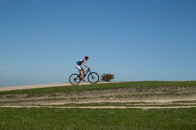 Rear view of man riding bicycle against clear blue sky