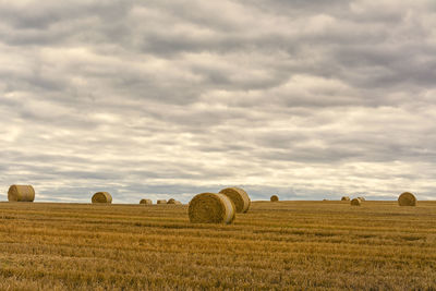 Hay bales on agricultural field against cloudy sky