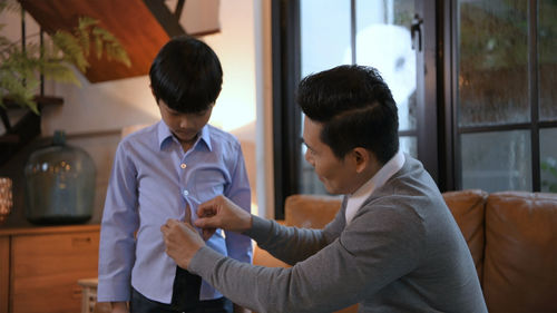 Father helping son to buttoning up shirt at home