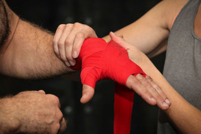 Midsection of man applying wristband on hand of boxer