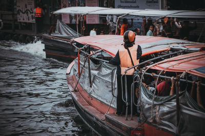 Rear view of man standing on boat moored in canal