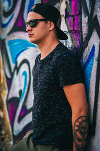 Young man wearing sunglasses leaning on graffiti wall