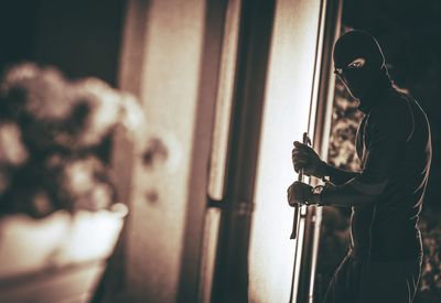 Side view portrait of male burglar holding crowbar at night