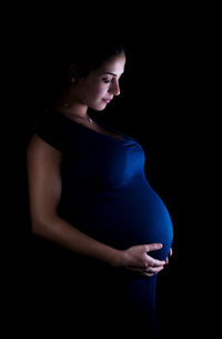 Pregnant woman with hands on stomach standing against black background