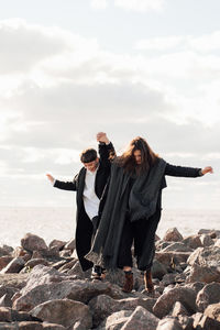 Lesbian women holding hands while walking on rock against sea and sky