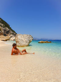 Shirtless man looking away while relaxing at beach