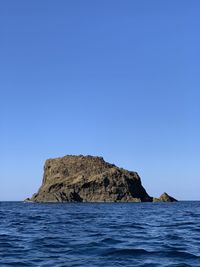Rock formation in sea against clear blue sky