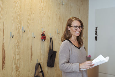 Smiling confident businesswoman holding documents while standing at office