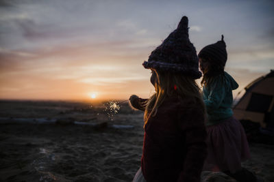 Sisters playing with sparkler while camping at beach during sunset