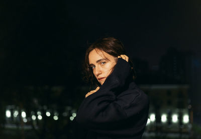 Portrait of beautiful young woman standing against illuminated at night