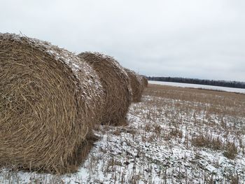 Hay bales on field against sky during winter