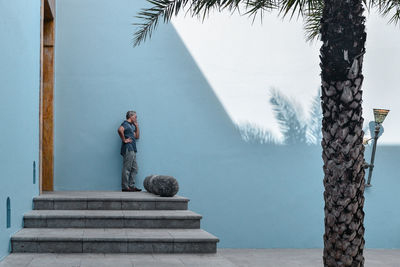 Mature man talking on phone while standing against blue wall