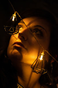 Close-up of woman by illuminated lighting equipment in darkroom