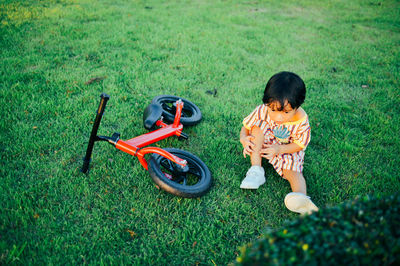 Boy sitting by cycle on grass