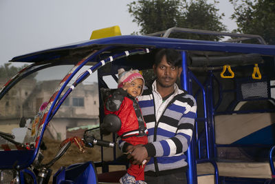 Portrait of man with son standing by vehicle outdoors