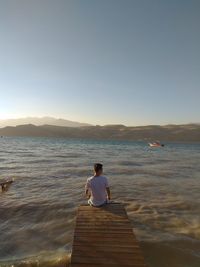 Rear view of man looking at sea against clear sky