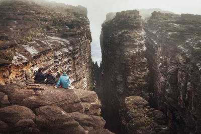 Rear view of friends sitting on rocky cliff