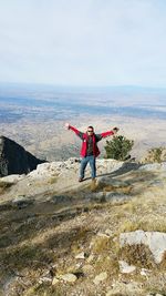 Man with arms outstretched standing against landscape