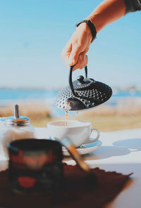 Close-up of hand holding drink at beach against sky