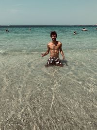 Full length of shirtless man in sea against sky