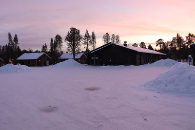 Houses on snow covered landscape against sky during sunset